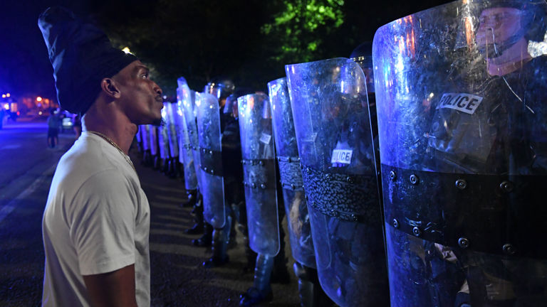 A man faces a row of police officers holding shields.