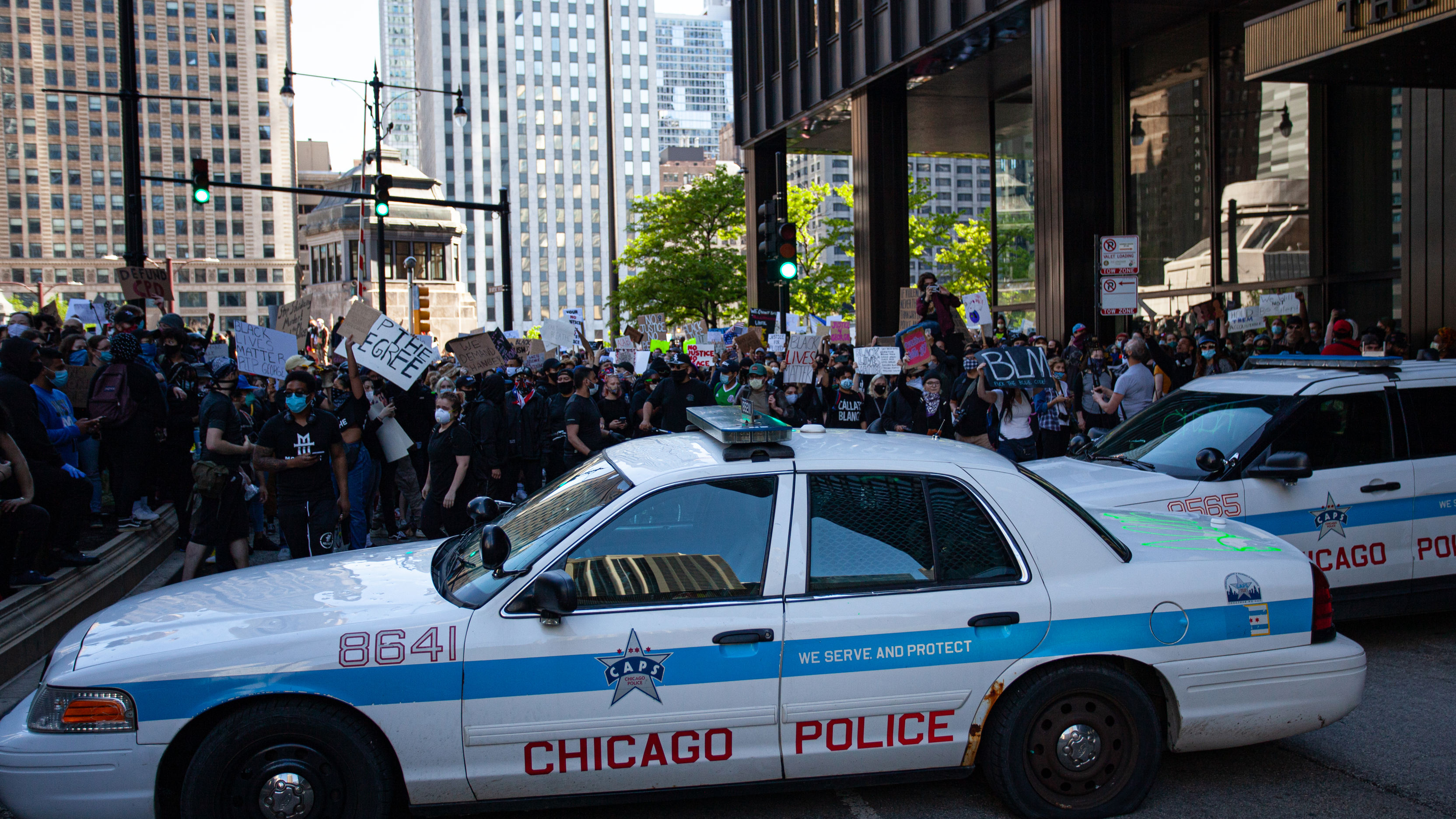 Behind a Chicago Police Department car, protestors rally for racial justice.