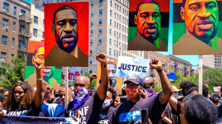 Protestors raise fists and hold signs with the face of George Floyd on them.