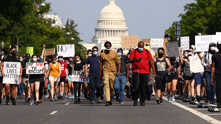 Protestors carrying racial justice signs march away from the U.S. Capitol Building.