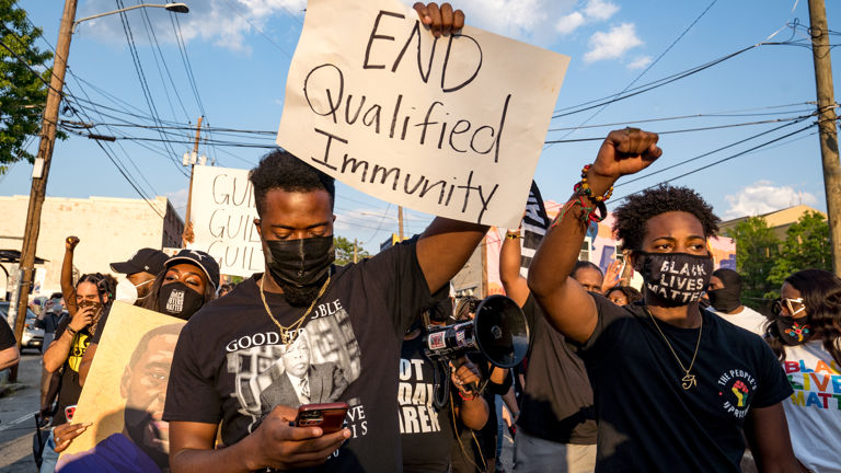 A protestor holds a sign reading "End qualified immunity" 