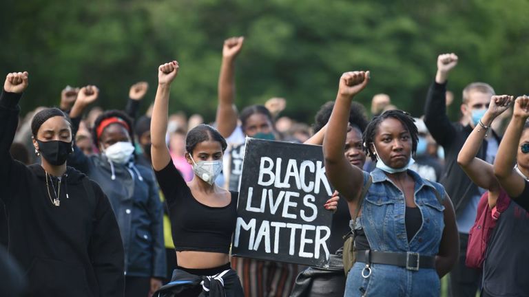 Protestors raise their fists and one holds a sign reading "Black Lives Matter"
